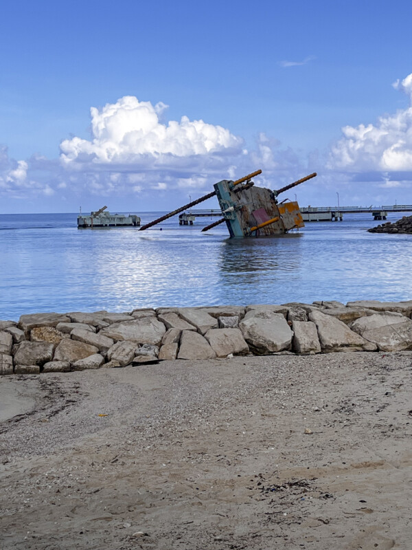 A dock lists into the harbor, rebar exposed, with sections of the pier collapsed behind it.